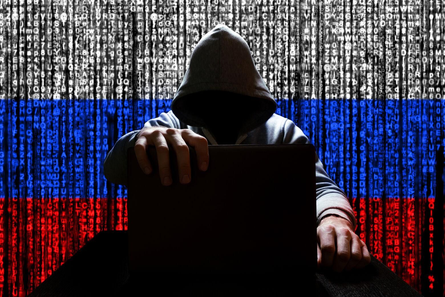 Hooded man with laptop on a background of the Russian flag in glitchy code